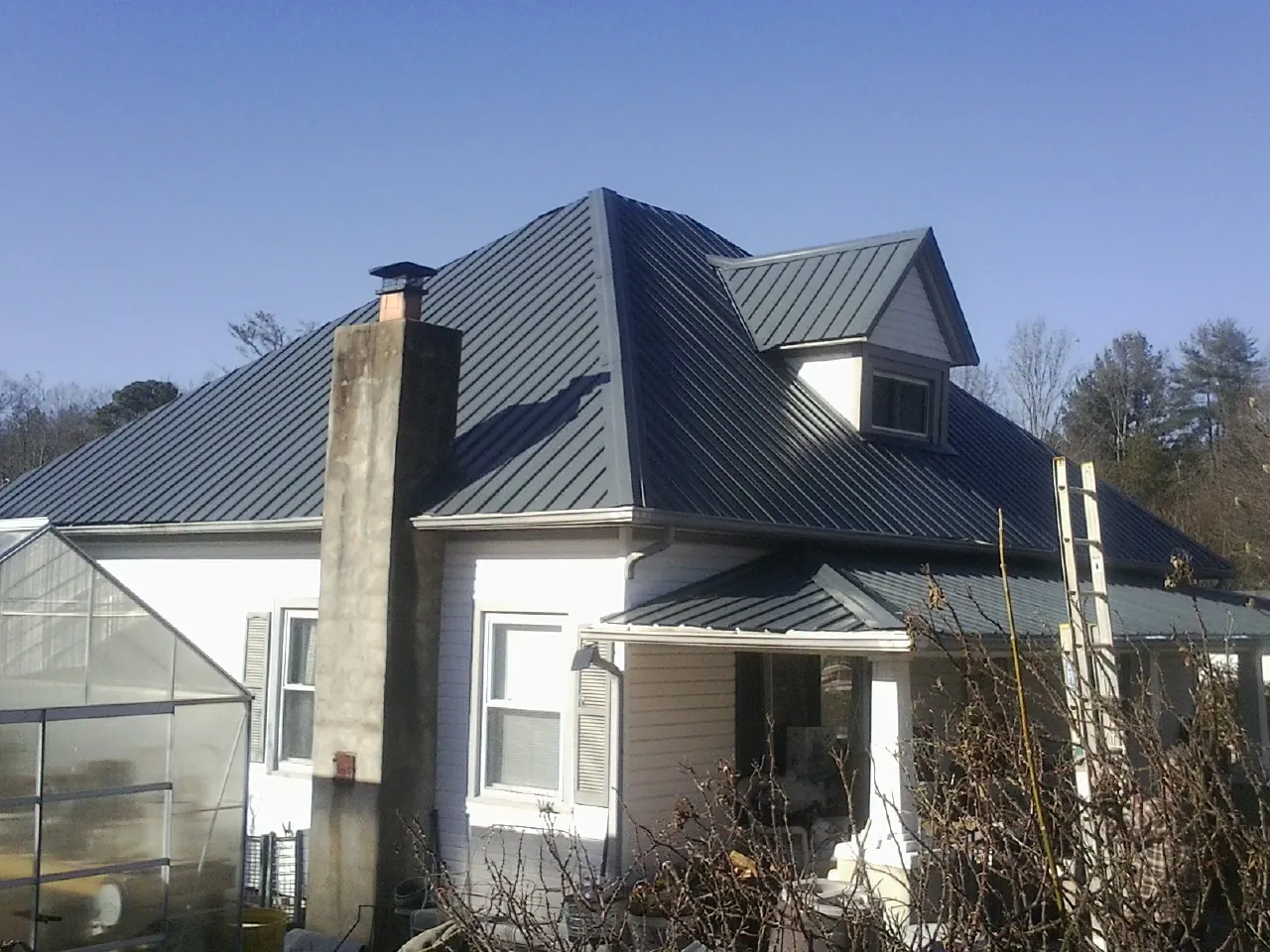 Dark blue standing seam metal roof on a white farmhouse with dormer — Slate & Tile Roof Repair by Roofing Brothers in Drury