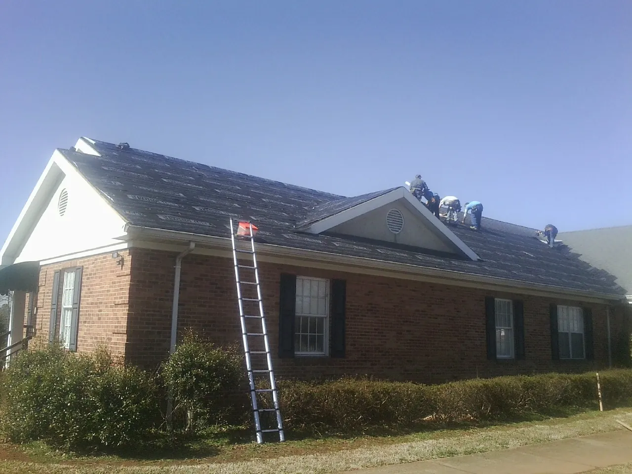 Crew tearing shingles off a brick ranch roof with a ladder set — Metal Roof Repair work by our crew in Drury