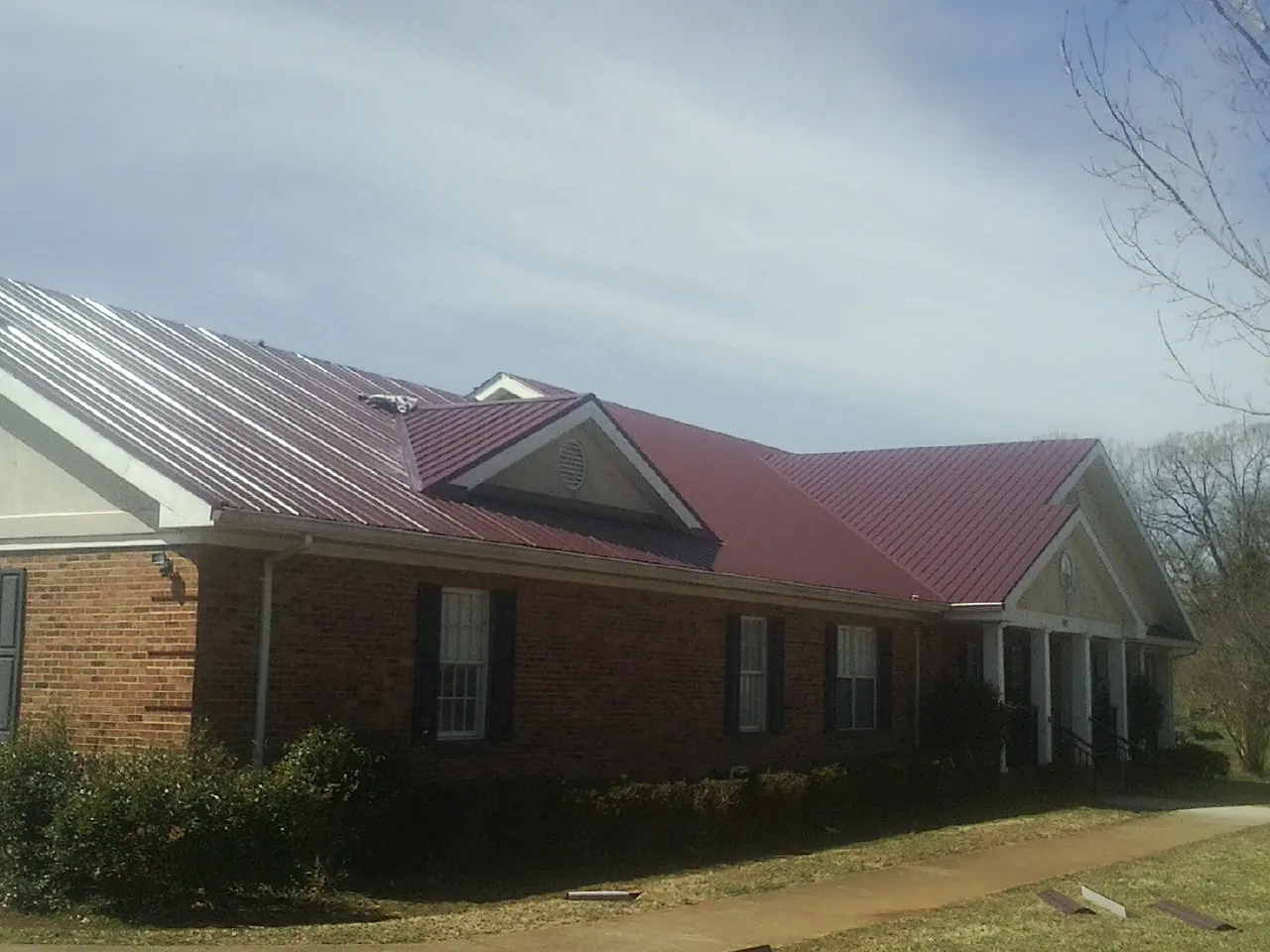 Red metal roof with gabled entries on a long brick building, from a Hail Damage Roof Repair job in Drury