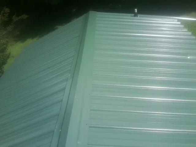 New green metal panels meeting at the ridge of a roof — Flat Roof Repair work by our crew in Drury