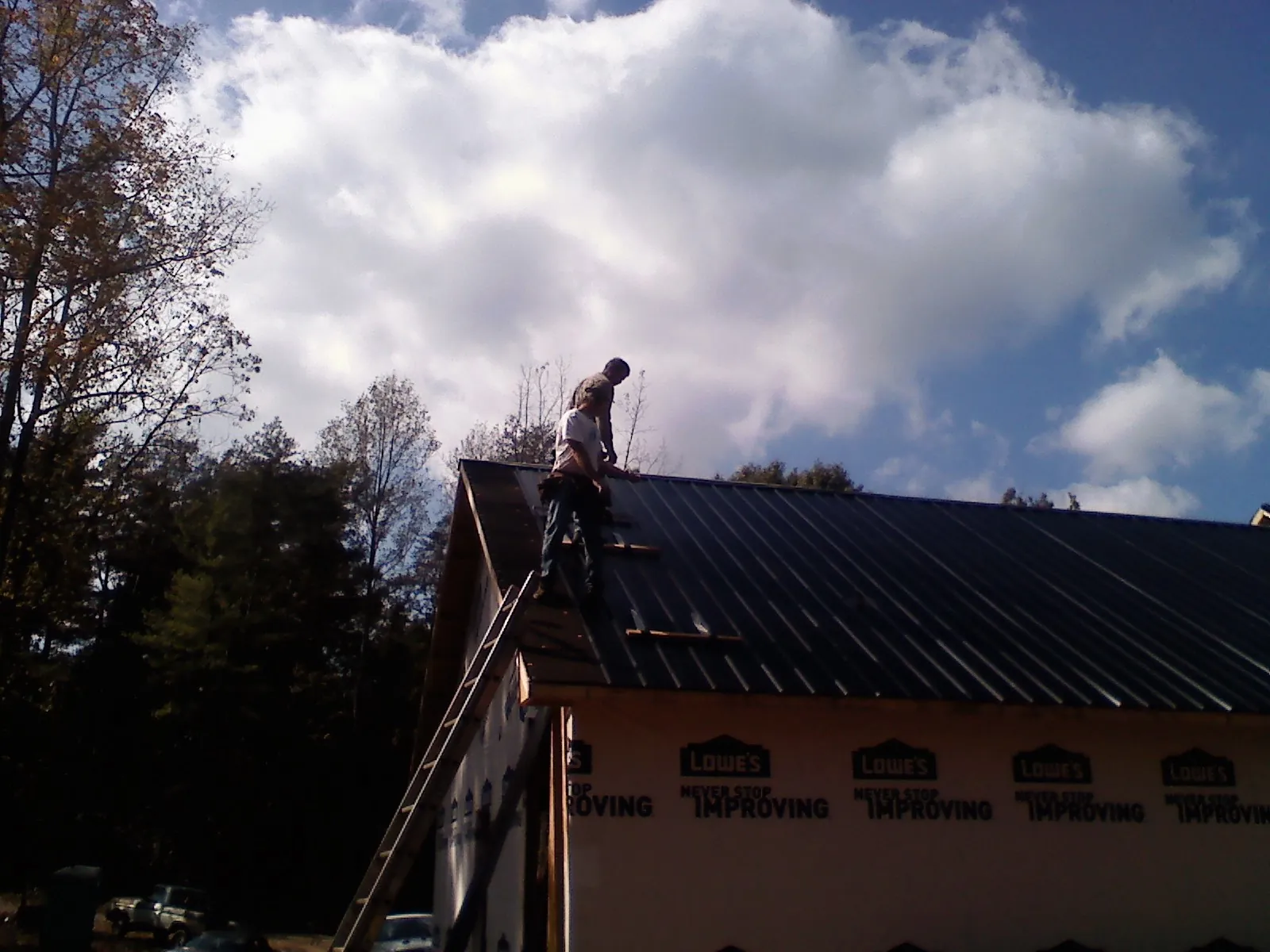 Roofer fastening dark metal panels high against a cloudy sky, from a Roof Inspection job in Drury