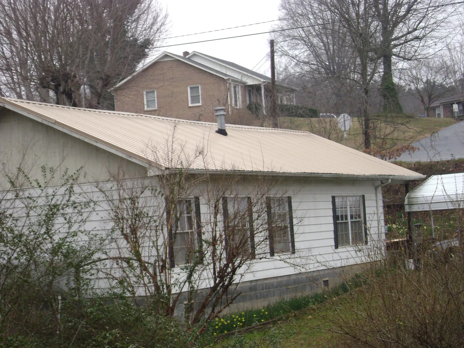 Tan metal roof on a white sided house set into a hillside — Commercial Roofing by Roofing Brothers in Drury