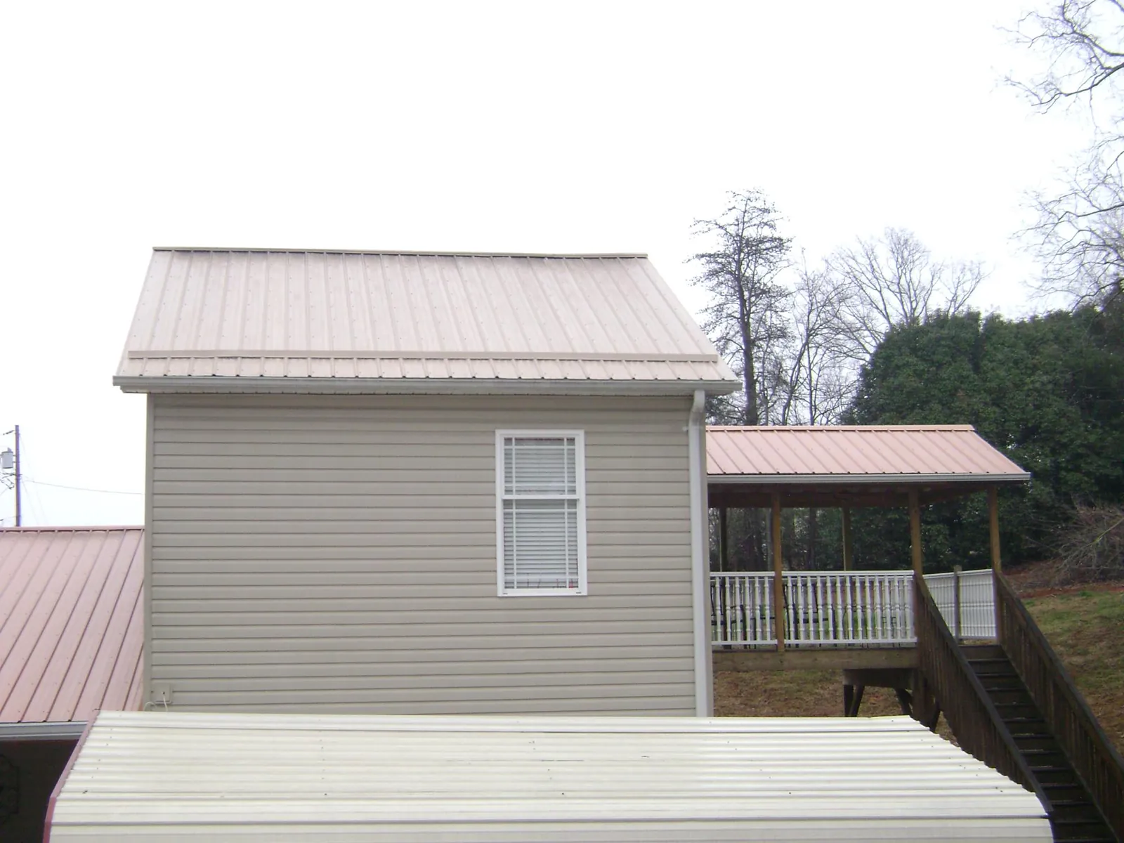 Tan metal roofs on a two story addition and attached porch, from a Roof Replacement job in Drury